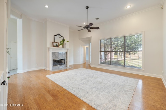 unfurnished living room featuring crown molding, a high end fireplace, light hardwood / wood-style floors, and ceiling fan