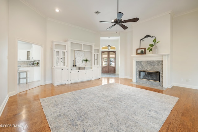 unfurnished living room with a towering ceiling, ornamental molding, a fireplace, and light wood-type flooring