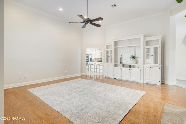 unfurnished living room featuring ceiling fan, ornamental molding, light hardwood / wood-style flooring, and a high ceiling