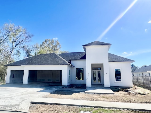 view of front of home with driveway, a shingled roof, stucco siding, french doors, and a garage