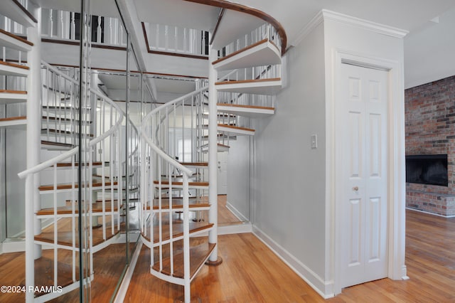 stairway featuring a fireplace, brick wall, hardwood / wood-style flooring, and crown molding