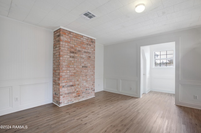 empty room featuring hardwood / wood-style floors, brick wall, and crown molding