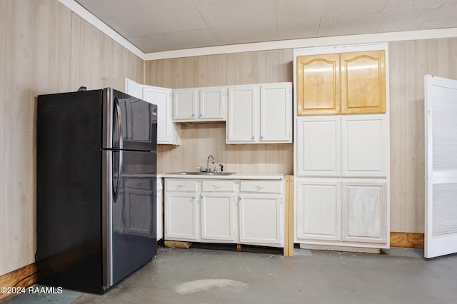 kitchen featuring white cabinetry, black fridge, wooden walls, and sink