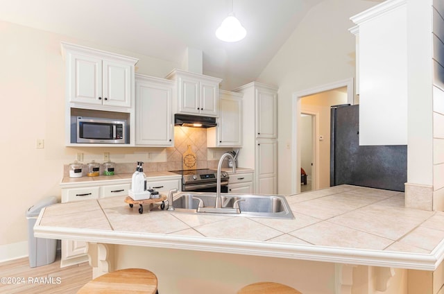 kitchen featuring tile countertops, white cabinetry, appliances with stainless steel finishes, a kitchen breakfast bar, and hanging light fixtures