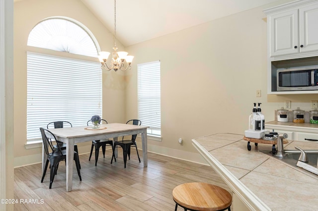 dining space featuring light wood-type flooring, a wealth of natural light, a chandelier, and vaulted ceiling