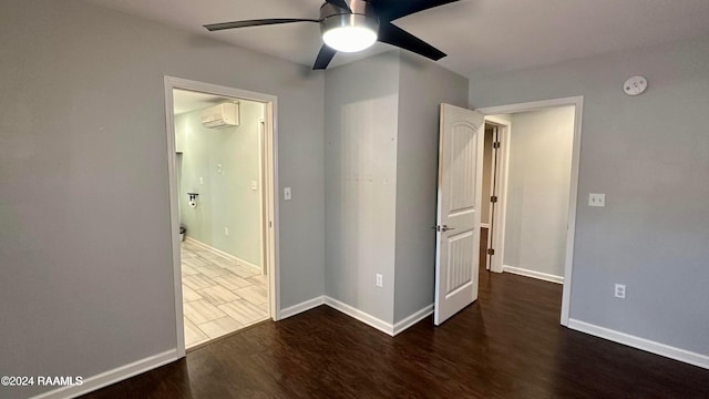 unfurnished bedroom featuring a wall unit AC, dark hardwood / wood-style flooring, and ceiling fan