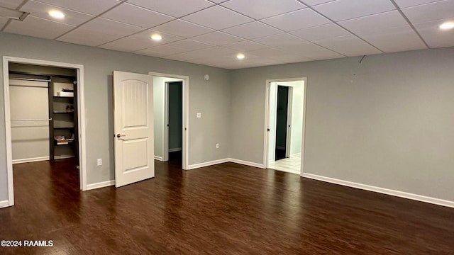 unfurnished bedroom featuring dark wood-type flooring, a paneled ceiling, a closet, and a walk in closet