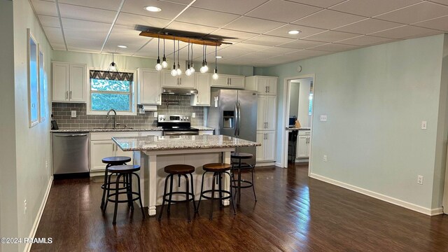 2213 Mills St, Lafayette, LA 70507 - kitchen featuring appliances with stainless steel finishes, under cabinet range hood, dark wood-style flooring, a kitchen breakfast bar, and a kitchen island