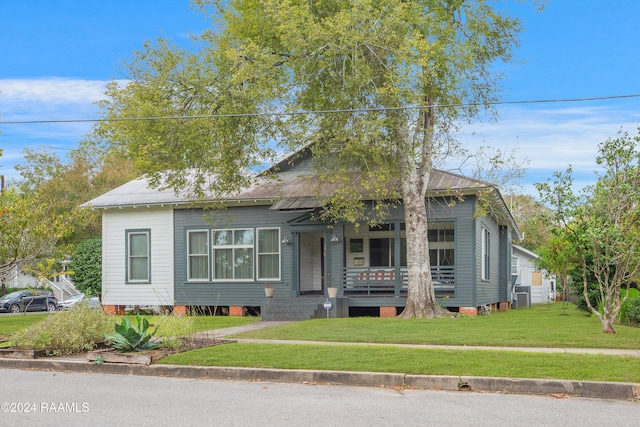 bungalow-style home featuring cooling unit, covered porch, and a front lawn