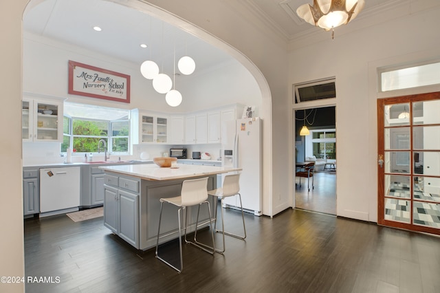 kitchen with white cabinetry, a center island, hanging light fixtures, ornamental molding, and white appliances