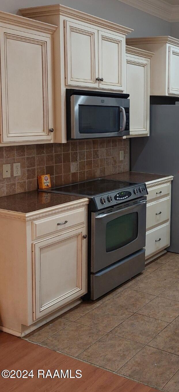 kitchen with decorative backsplash, stainless steel appliances, cream cabinets, and crown molding