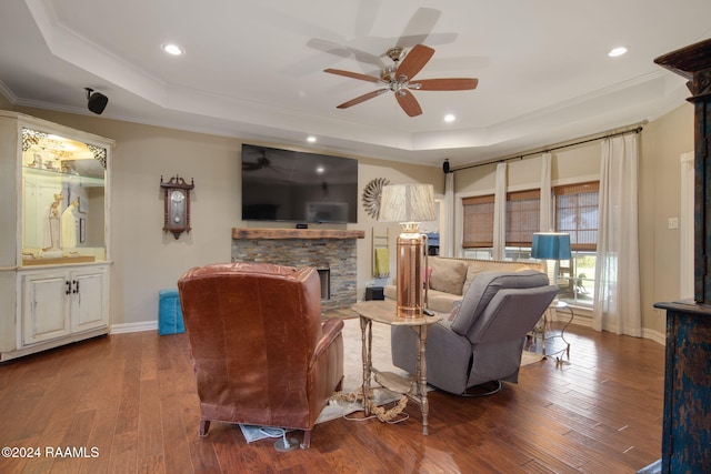 living room with a stone fireplace, wood-type flooring, crown molding, and a raised ceiling