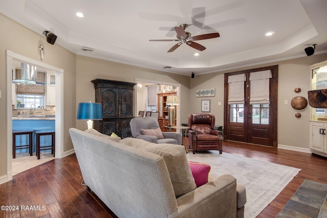 living room featuring dark hardwood / wood-style flooring, sink, ornamental molding, ceiling fan, and a tray ceiling