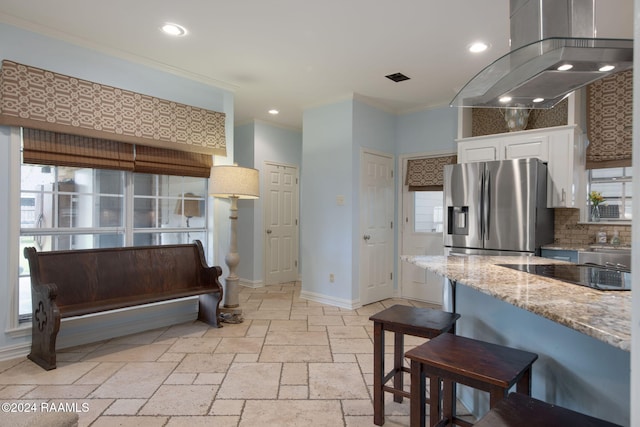 kitchen featuring light stone counters, stainless steel refrigerator with ice dispenser, a kitchen bar, island range hood, and crown molding