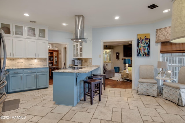 kitchen featuring island range hood, white cabinets, kitchen peninsula, a kitchen breakfast bar, and backsplash