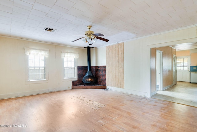 unfurnished living room with a wood stove, light hardwood / wood-style floors, ceiling fan, and crown molding