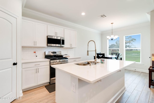 kitchen featuring appliances with stainless steel finishes, pendant lighting, sink, white cabinets, and a kitchen island with sink