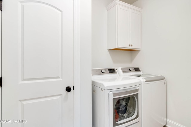 clothes washing area with separate washer and dryer and cabinets