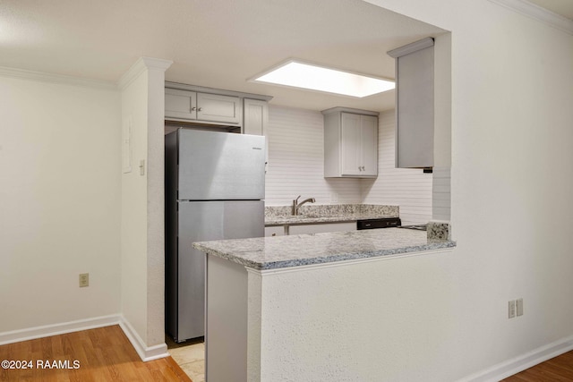 kitchen with kitchen peninsula, stainless steel fridge, light wood-type flooring, and sink