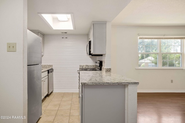 kitchen featuring a skylight, appliances with stainless steel finishes, light hardwood / wood-style floors, light stone counters, and kitchen peninsula