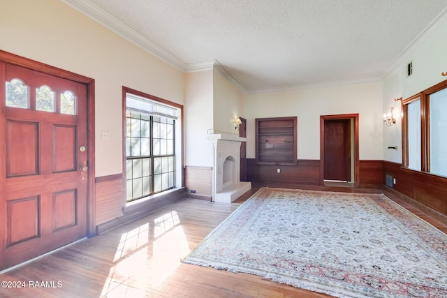 entrance foyer with light wood-type flooring, a textured ceiling, crown molding, and wood walls