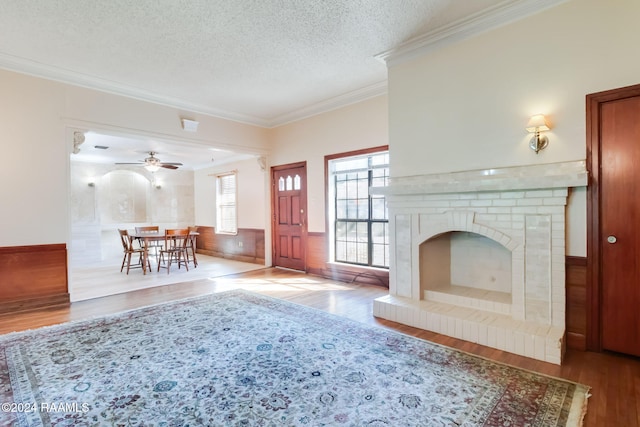 unfurnished living room featuring light wood-type flooring, a textured ceiling, crown molding, a fireplace, and wood walls