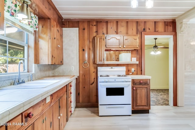 kitchen featuring light wood-type flooring, gas range gas stove, ceiling fan, sink, and tile countertops