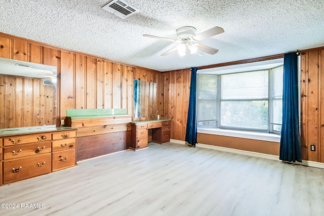 interior space featuring a textured ceiling, light wood-type flooring, ornamental molding, and wood walls