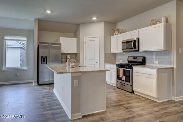 kitchen featuring hardwood / wood-style flooring, appliances with stainless steel finishes, light stone countertops, a kitchen island with sink, and white cabinets