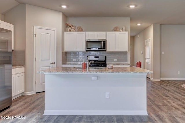 kitchen with stainless steel appliances, light hardwood / wood-style floors, white cabinetry, and a kitchen island with sink