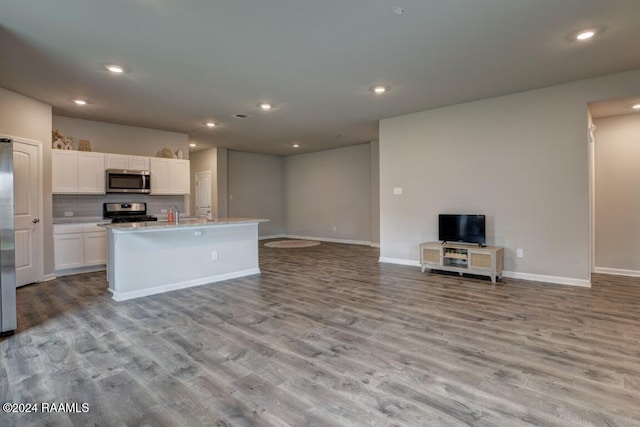 kitchen with stainless steel appliances, white cabinetry, backsplash, an island with sink, and light hardwood / wood-style flooring