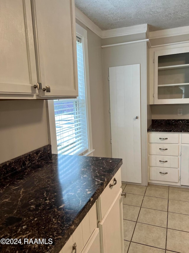 kitchen featuring ornamental molding, dark stone counters, a textured ceiling, light tile patterned floors, and white cabinets