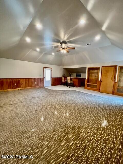 bonus room with carpet floors, ceiling fan, vaulted ceiling, and wooden walls