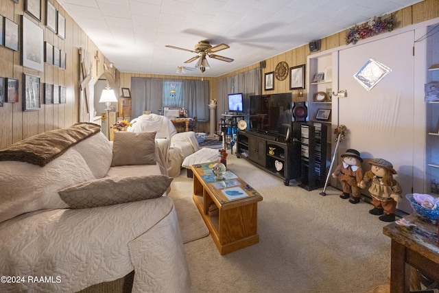 living room featuring ceiling fan, light carpet, and wood walls