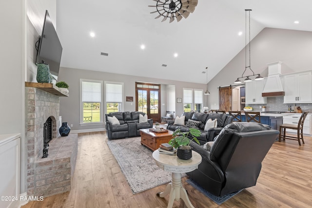 living room featuring light wood-type flooring, ceiling fan, a barn door, high vaulted ceiling, and a fireplace