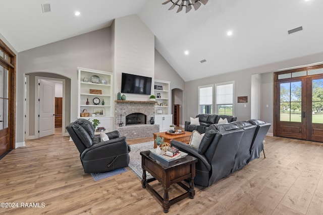 living room featuring a healthy amount of sunlight, a fireplace, high vaulted ceiling, and light hardwood / wood-style flooring