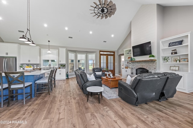 living room featuring ceiling fan, sink, a stone fireplace, high vaulted ceiling, and light hardwood / wood-style floors