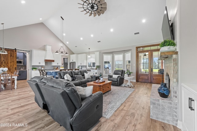 living room featuring a barn door, light wood-type flooring, high vaulted ceiling, and french doors