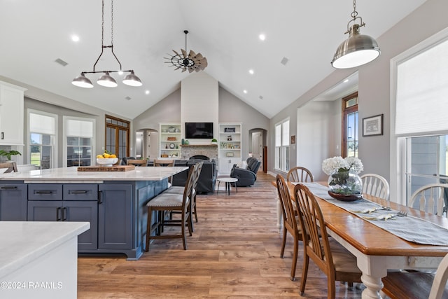 kitchen with gray cabinetry, high vaulted ceiling, light wood-type flooring, decorative light fixtures, and a large fireplace