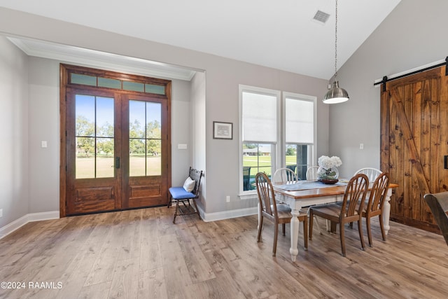 dining space featuring light hardwood / wood-style floors, a barn door, lofted ceiling, and crown molding