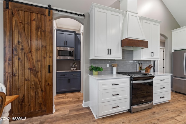 kitchen with premium range hood, stainless steel appliances, a barn door, light hardwood / wood-style flooring, and white cabinets