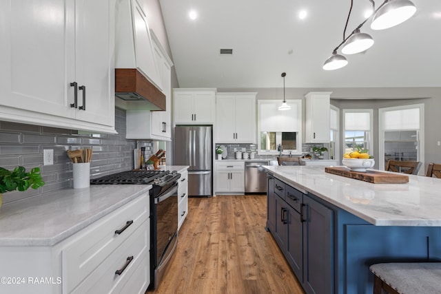 kitchen featuring custom exhaust hood, stainless steel appliances, pendant lighting, light hardwood / wood-style flooring, and white cabinets