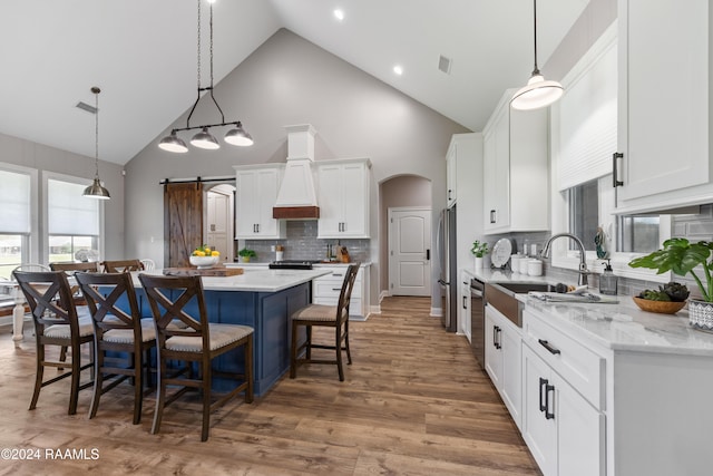 kitchen featuring high vaulted ceiling, a barn door, a kitchen island, white cabinetry, and stainless steel appliances