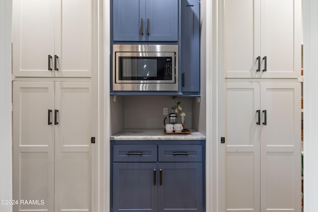 kitchen featuring white cabinets, stainless steel microwave, and blue cabinetry