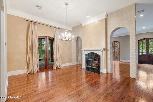 unfurnished living room featuring ornamental molding, a premium fireplace, wood-type flooring, and a notable chandelier