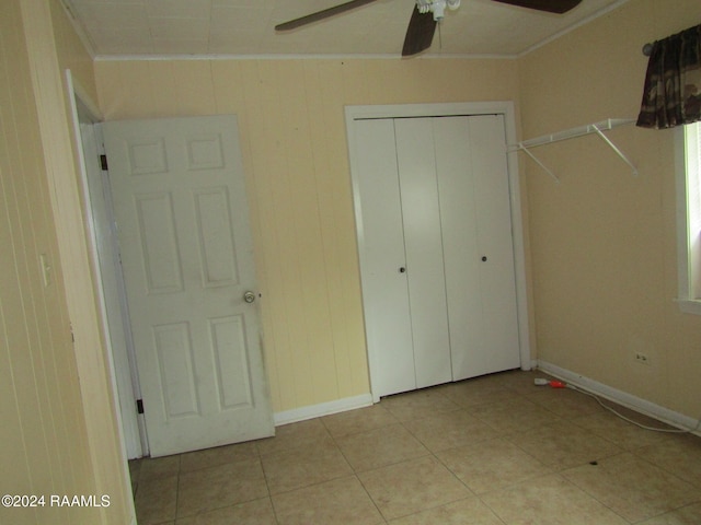 unfurnished bedroom with ornamental molding, wooden walls, ceiling fan, and a closet