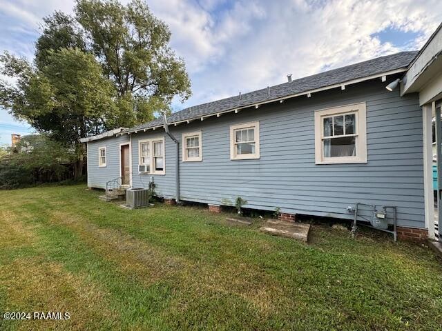 rear view of house with central air condition unit and a lawn