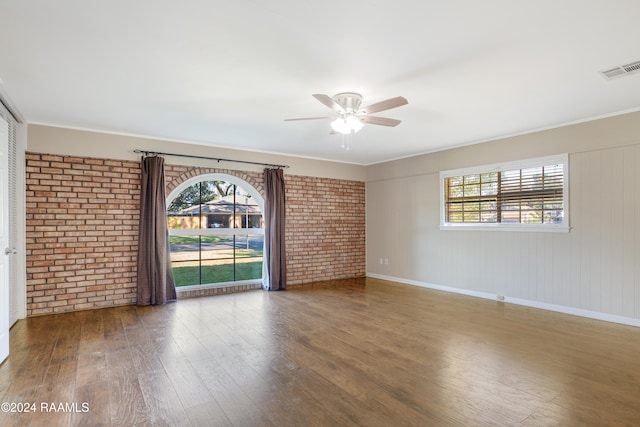 empty room featuring a wealth of natural light, brick wall, and hardwood / wood-style flooring