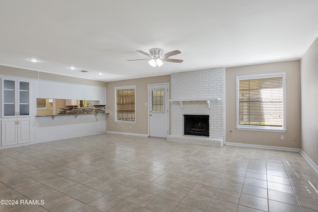 unfurnished living room featuring a brick fireplace, ceiling fan, and light tile patterned floors