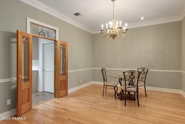 dining area with light wood-type flooring, an inviting chandelier, and ornamental molding